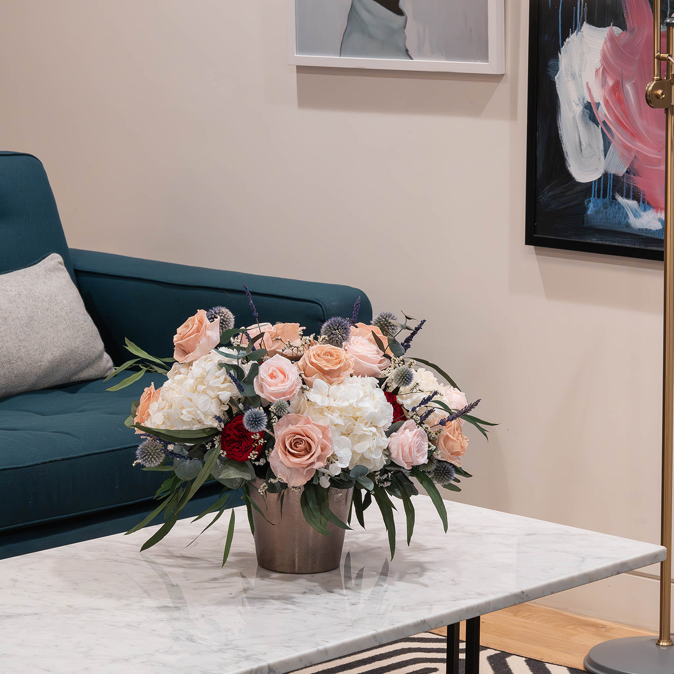 Preserved flower arrangement in a gold vase displayed in a modern office lobby seating area.