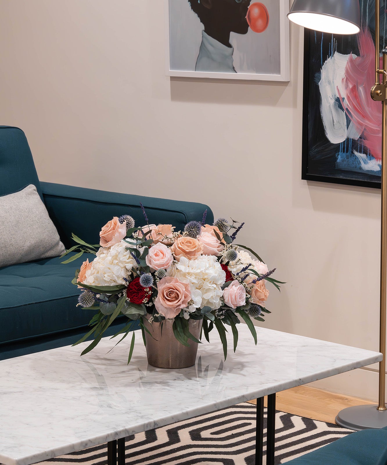 Preserved flower arrangement in a gold vase displayed in a modern office lobby seating area.