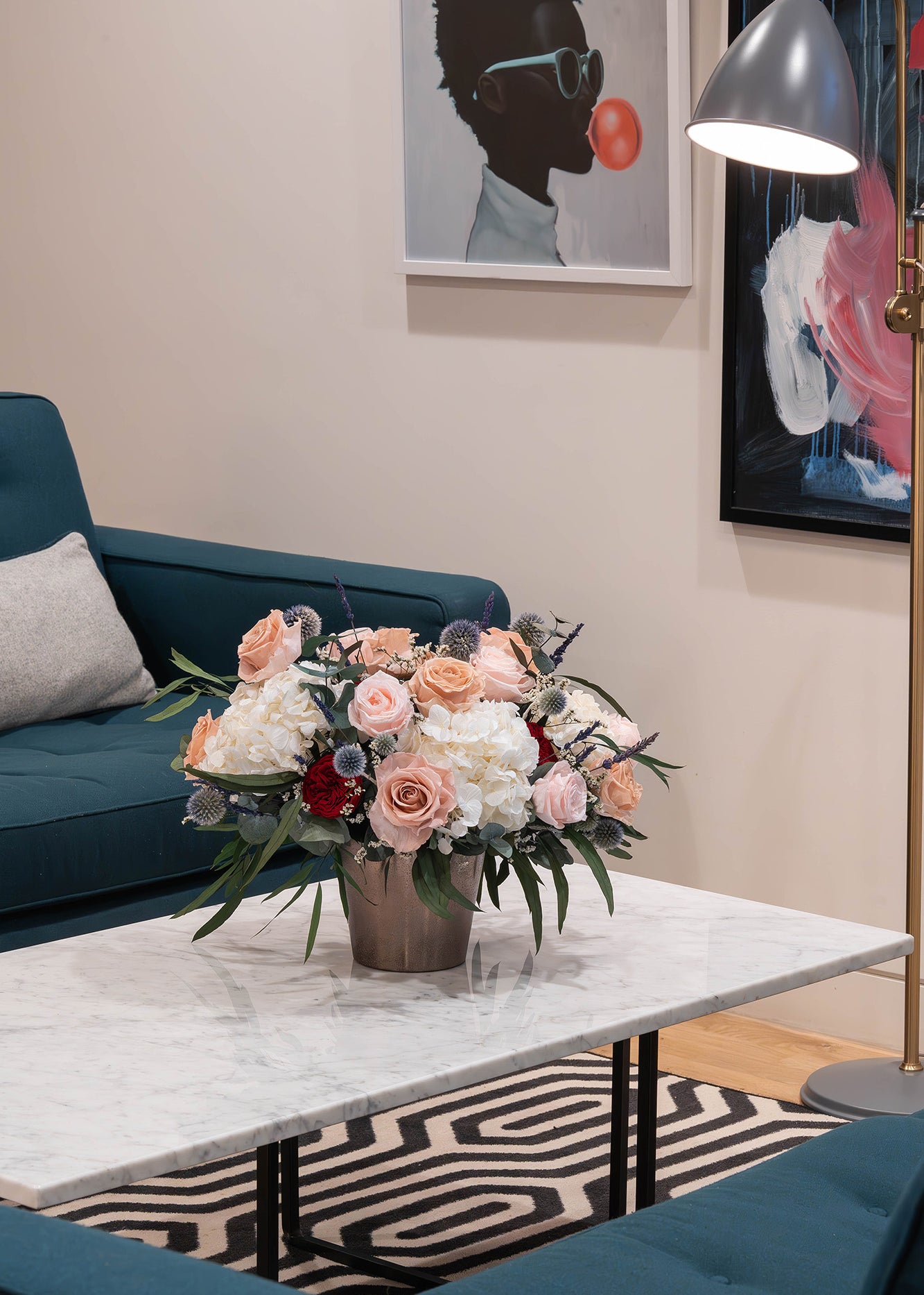 Preserved flower arrangement in a gold vase displayed in a modern office lobby seating area.