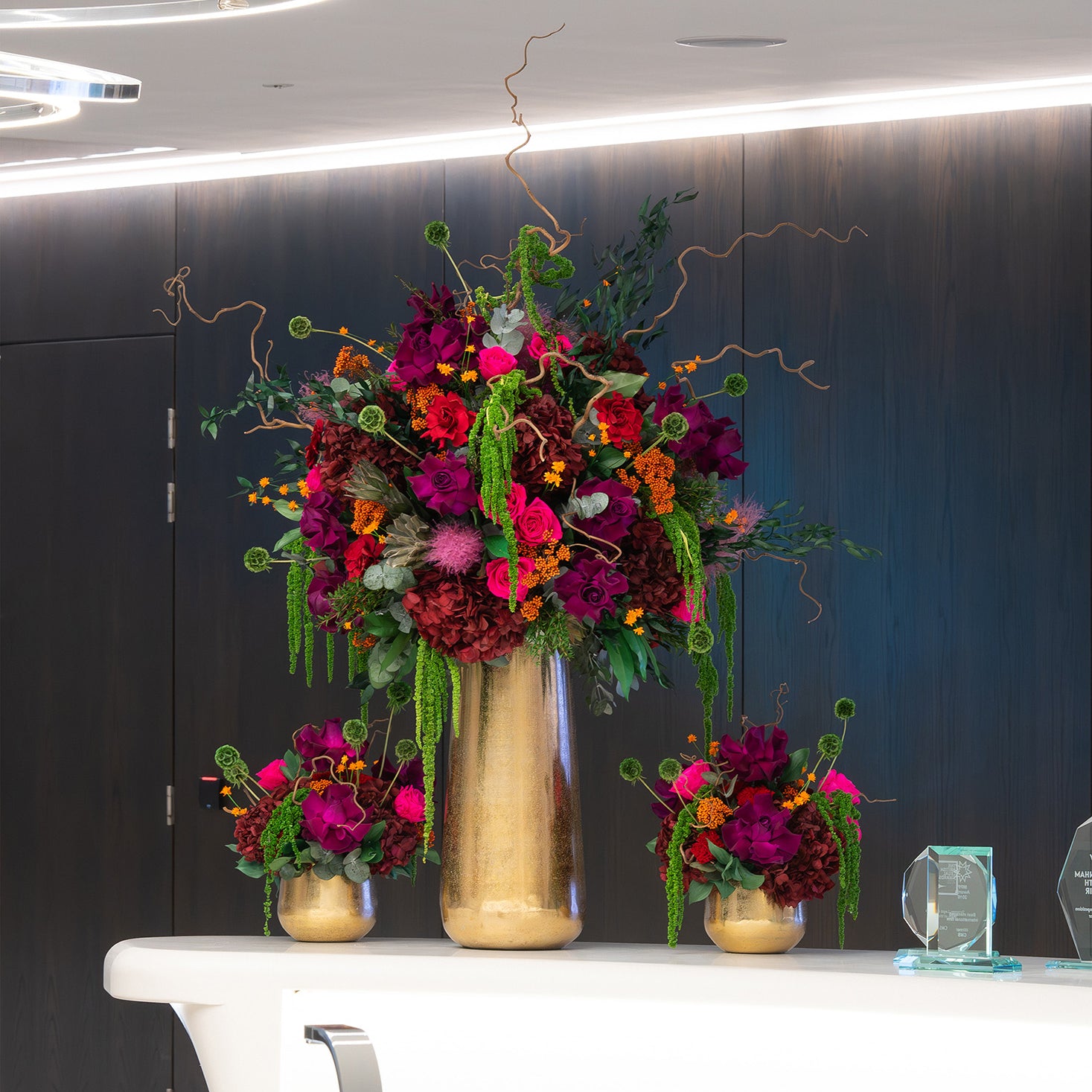 Preserved purple mixed flower arrangements in gold vases on office lobby table