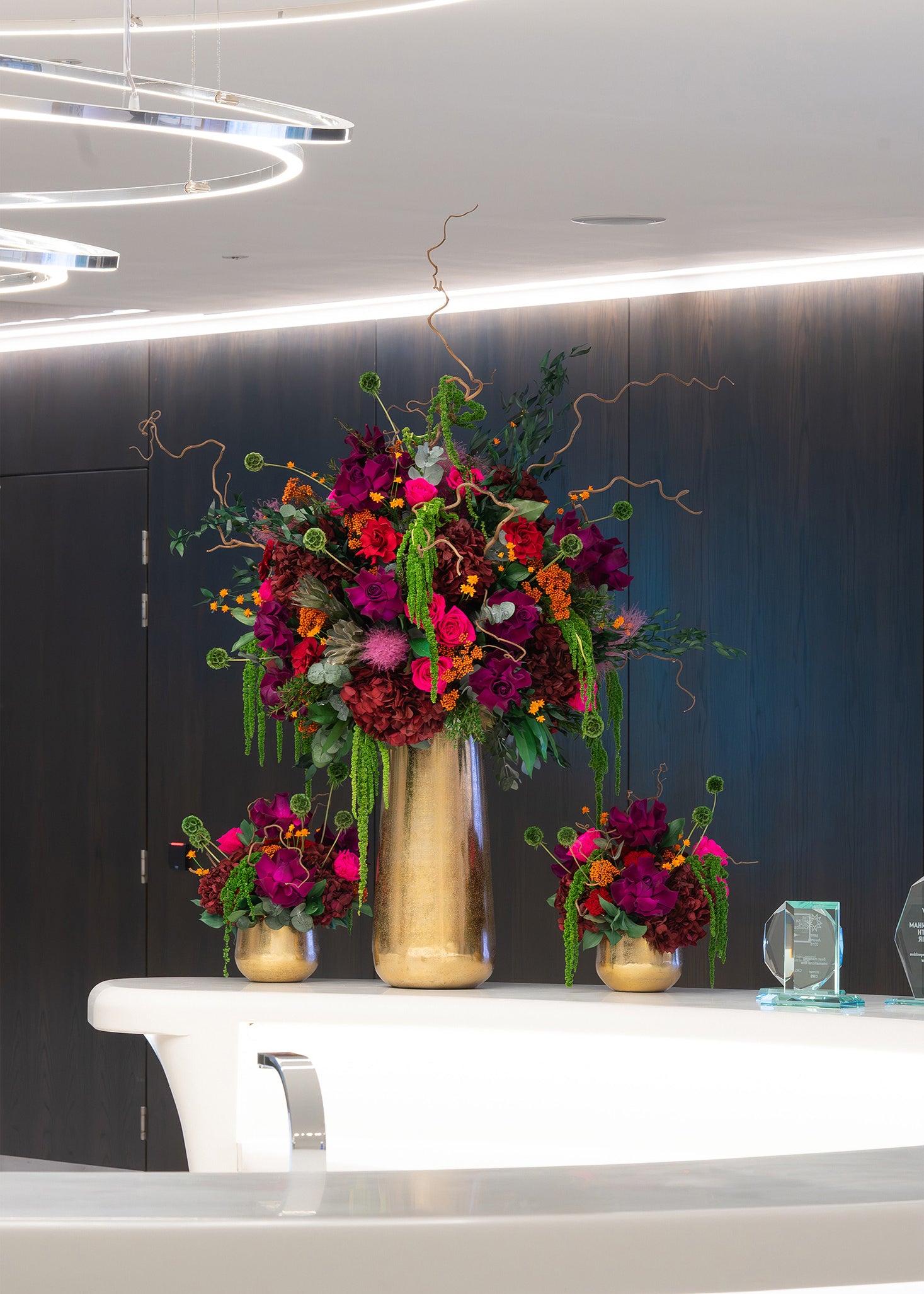 Preserved purple mixed flower arrangements in gold vases on office lobby table