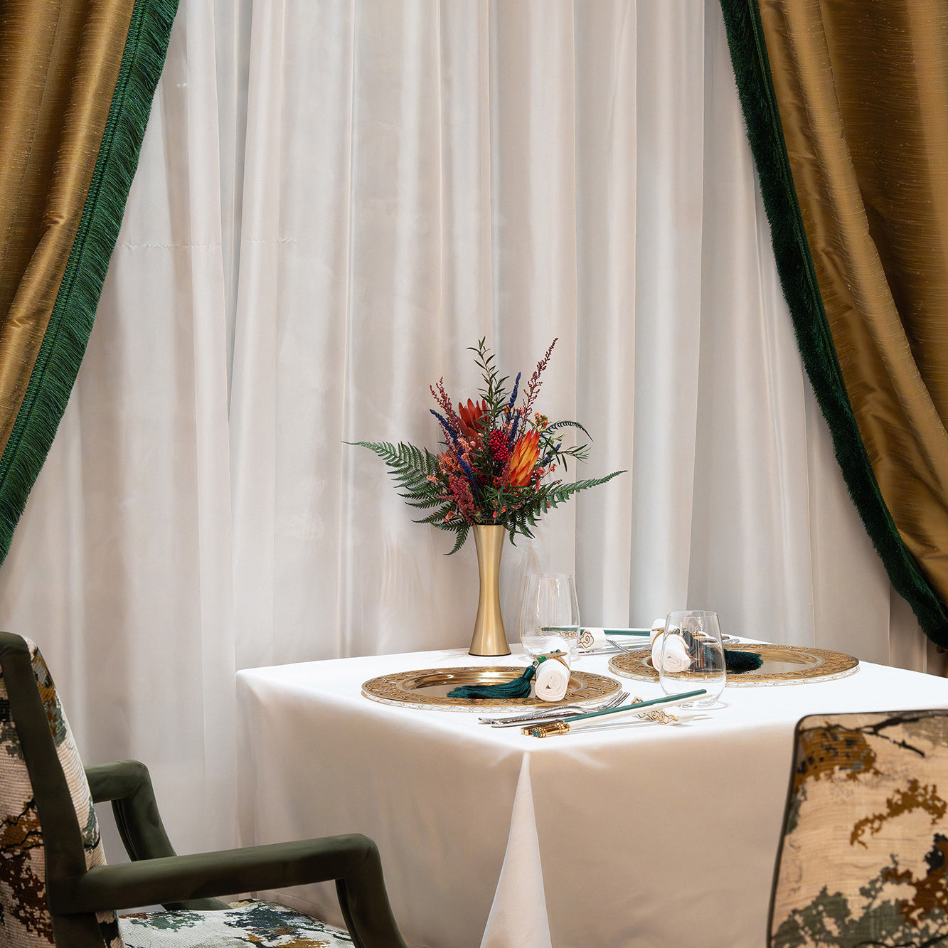An arrangement of preserved protea, fern, and eucalyptus displayed in a metallic vase inside a restaurant