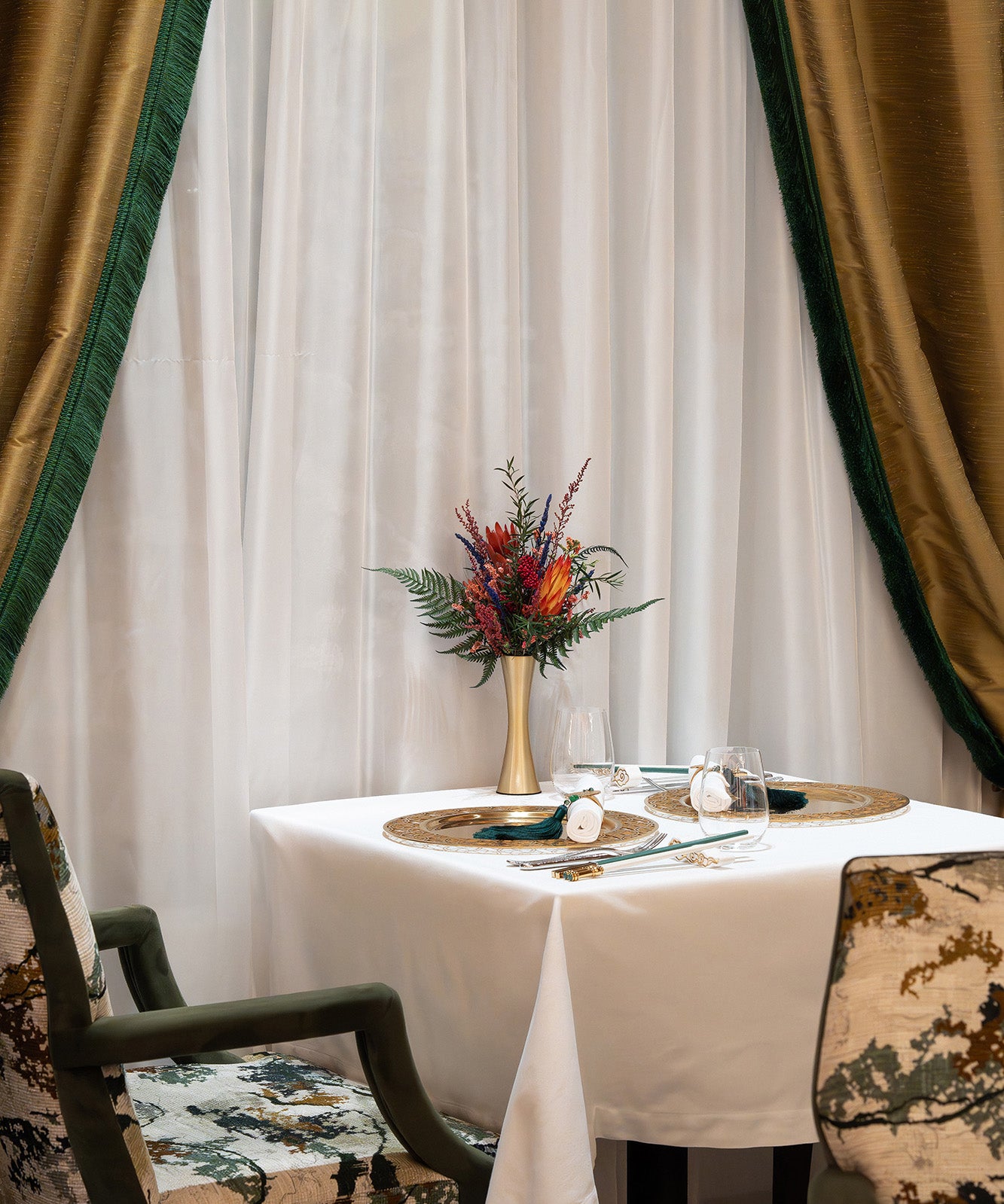 An arrangement of preserved protea, fern, and eucalyptus displayed in a metallic vase inside a restaurant