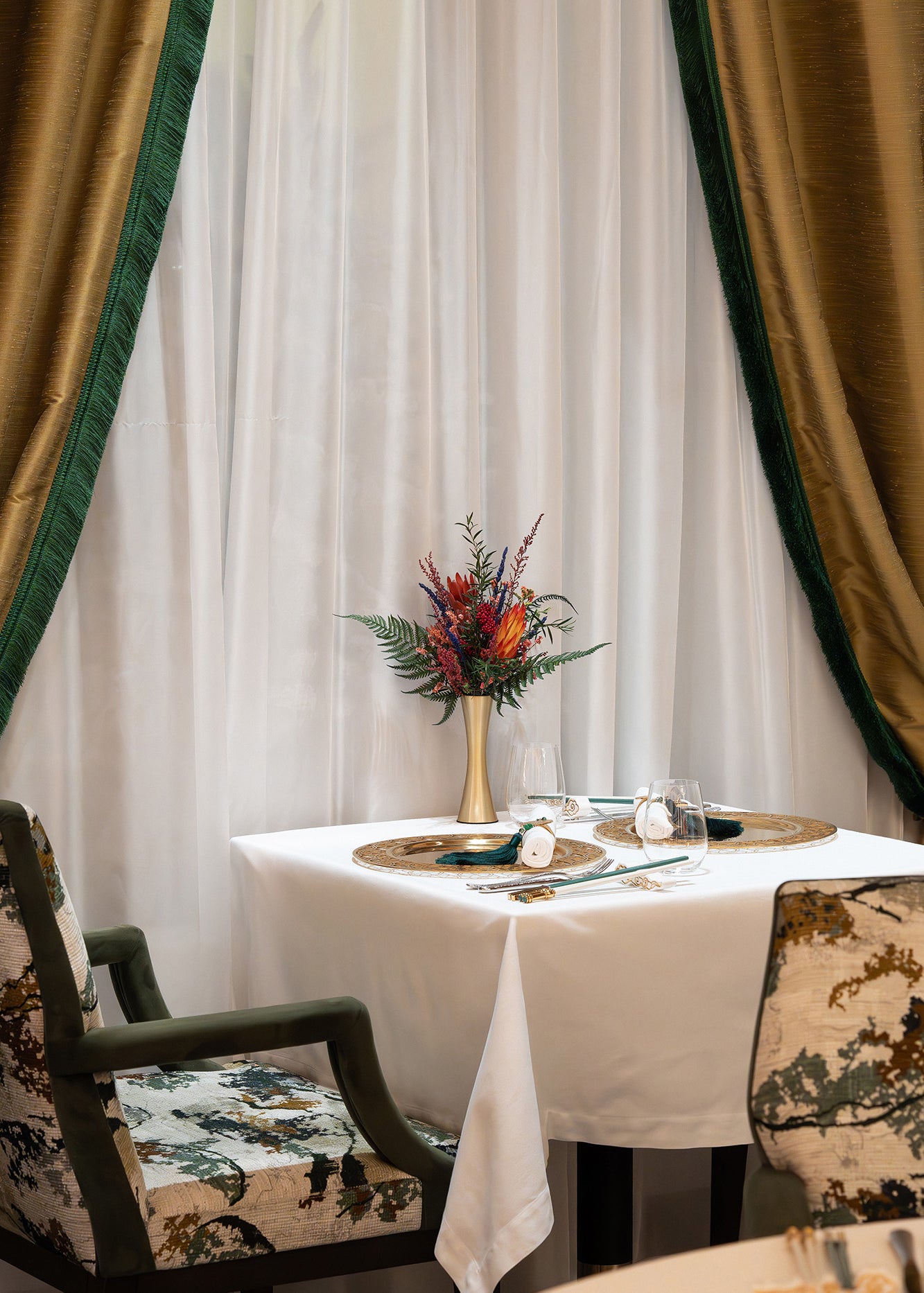 An arrangement of preserved protea, fern, and eucalyptus displayed in a metallic vase inside a restaurant