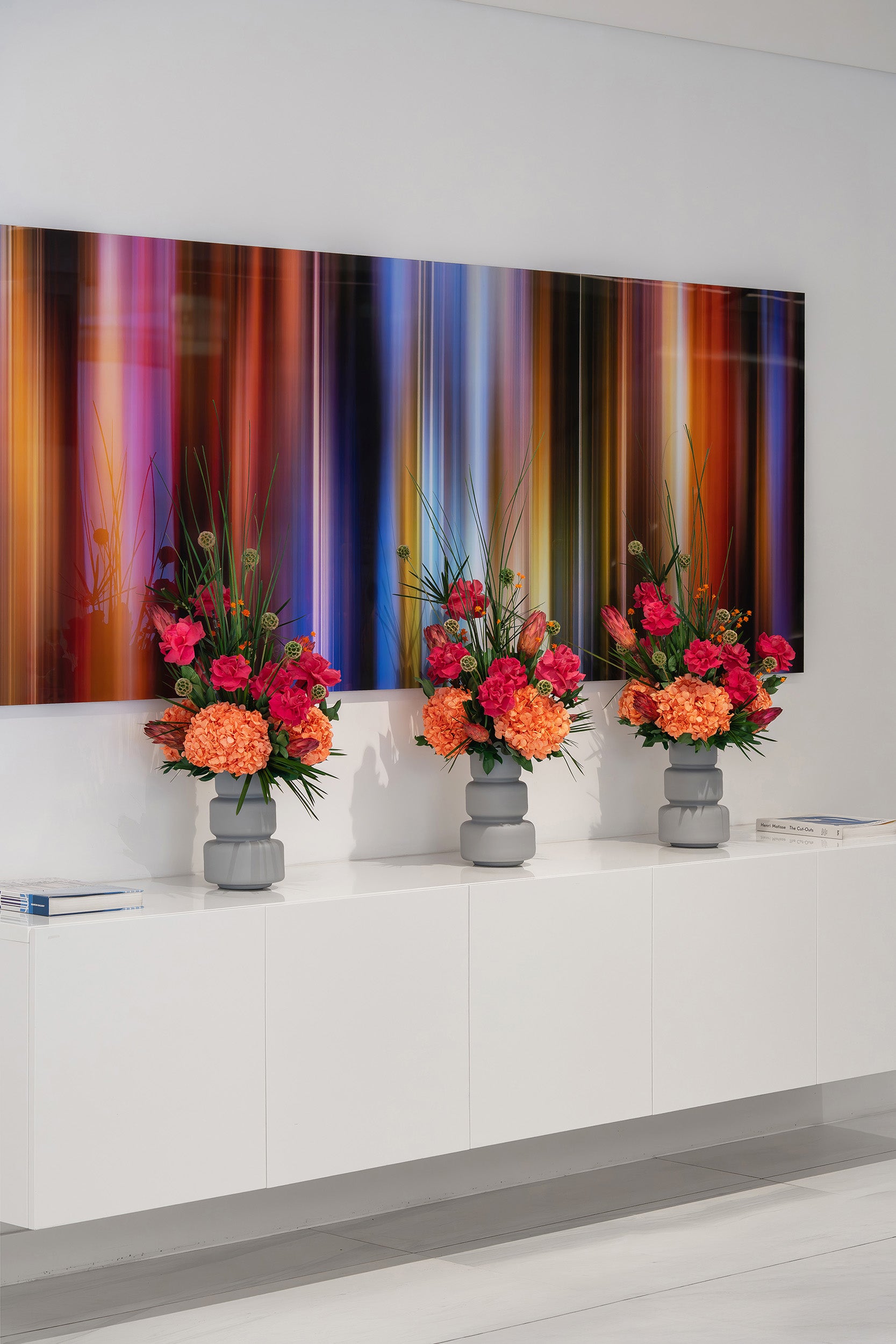 Three preserved mixed tropical flower arrangements on a white surface with a colourful abstract painting in the background.