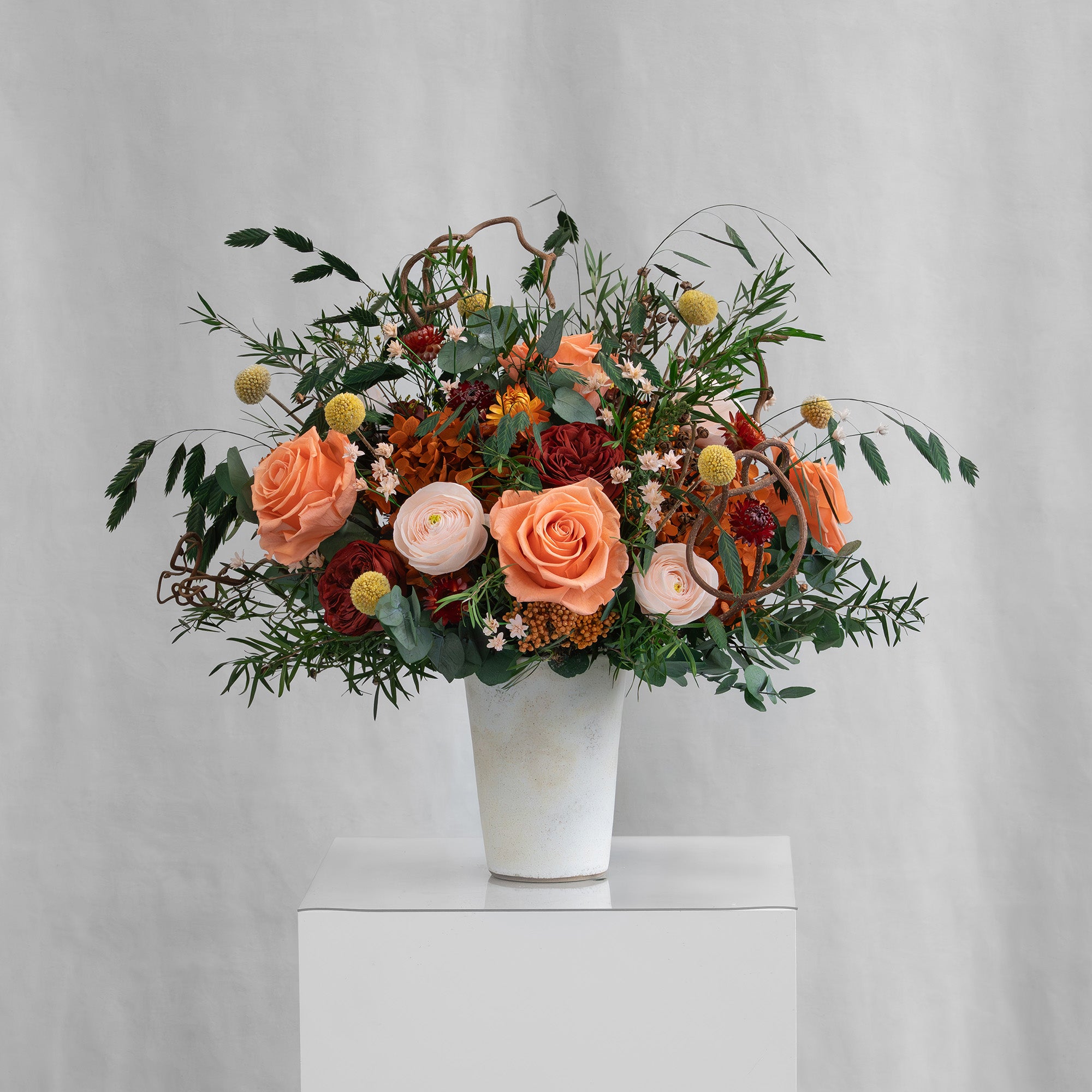 Preserved floral arrangement with orange, red, peach, and filler flowers in a ceramic handmade vase 