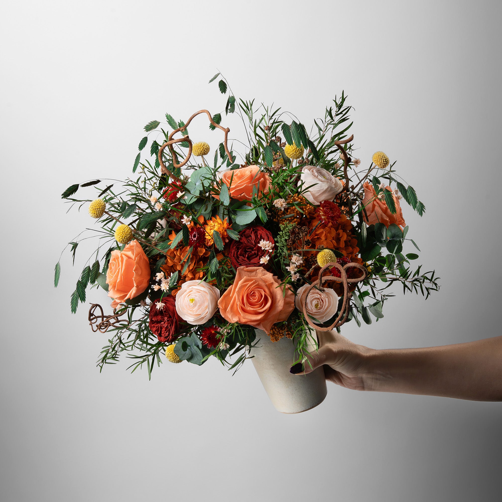 Preserved floral arrangement with orange, red, peach, and filler flowers in a ceramic handmade vase 