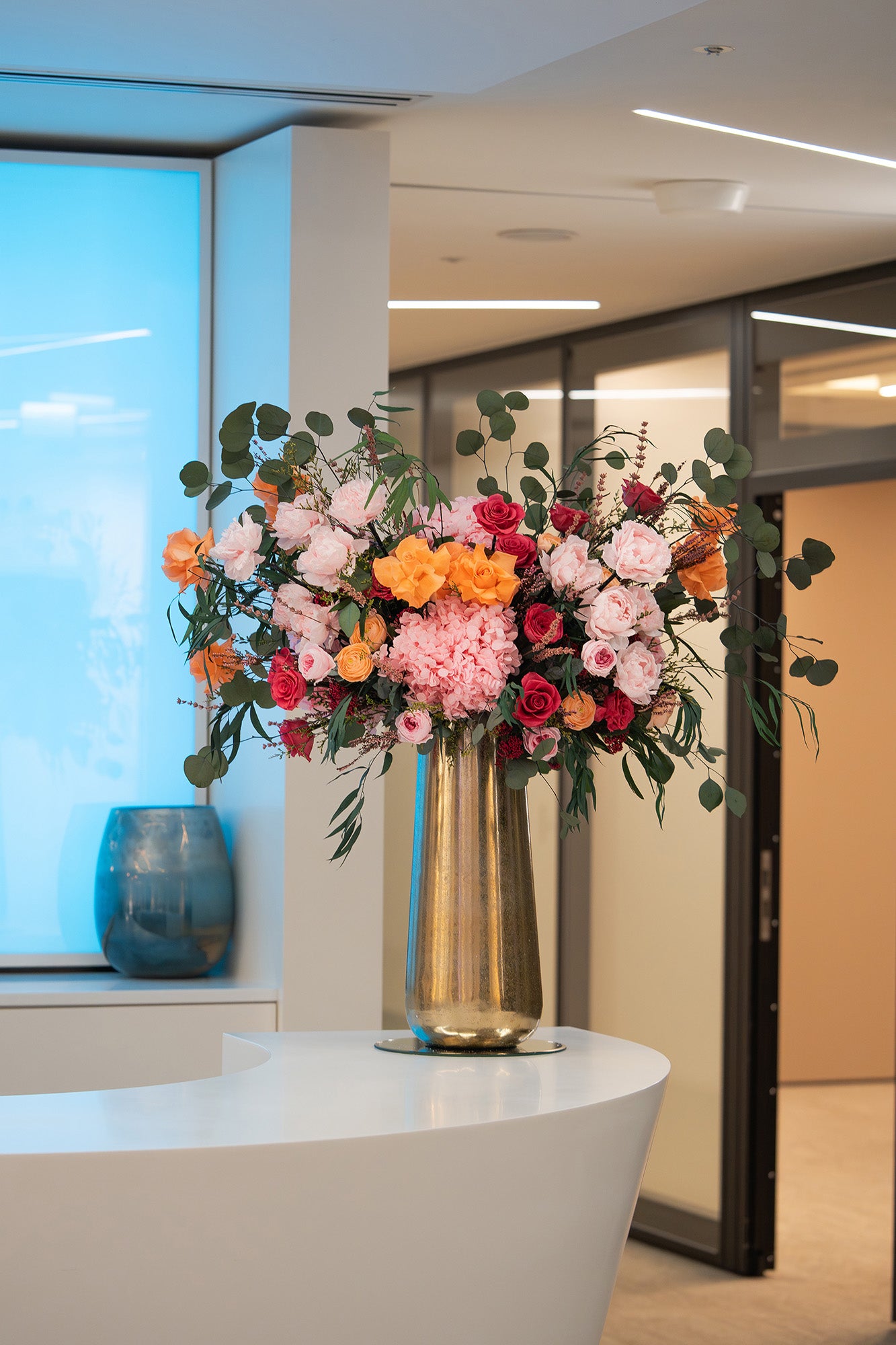 A colourful preserved flower arrangement displayed in a gold vase in an office lobby