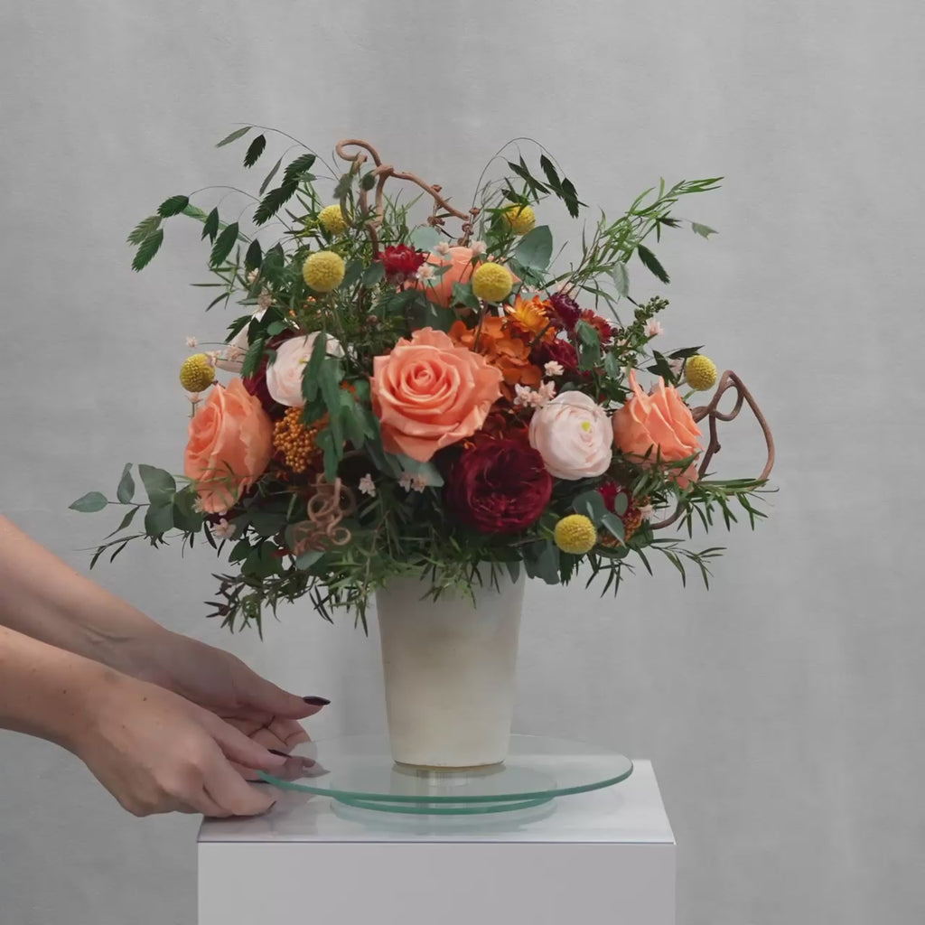 Preserved floral arrangement with orange, red, peach, and filler flowers in a ceramic handmade vase 